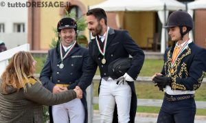 Podio del campionato italiano MCI M2 con sul gradino più alto del podio Umberto Paradisi che vediamo ricevere le congratulazioni da Adriana Foti, argento a Giacomo Mazzoleni e bronzo a Mattia Alghisi. (photo © tuttoDRESSAGE).